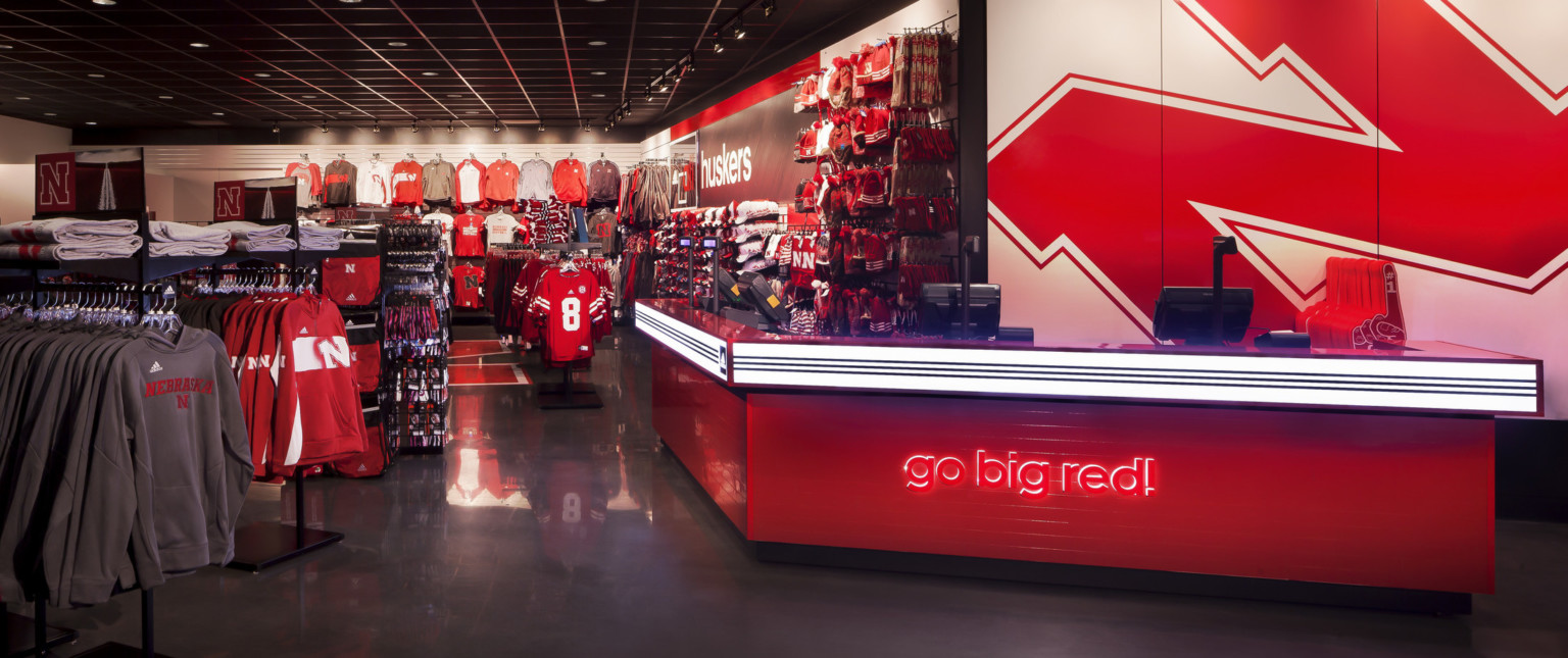 Retail space selling sports fan gear for the Nebraska Huskers. Illuminated red counter reads "Go big red!", Nebraska logo behind