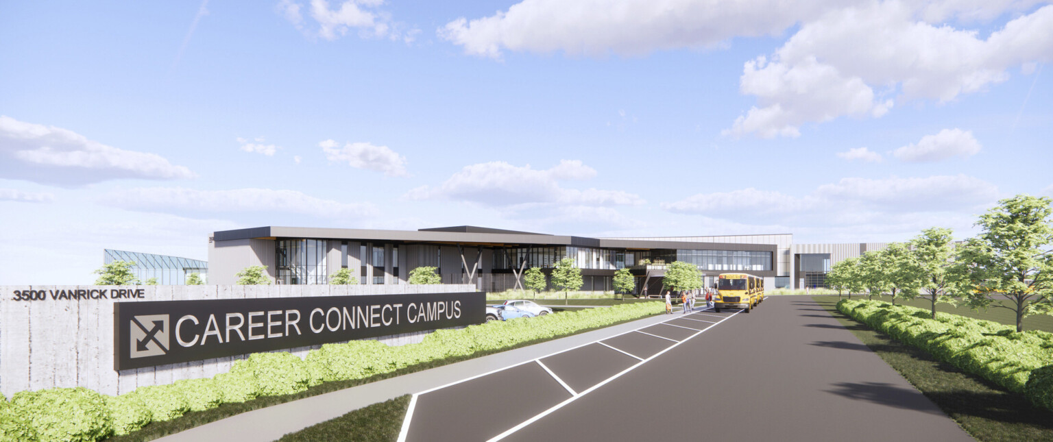 a traffic loop lined with landscaping and concrete signage wall leading to a mid rise school facility with a yellow bus