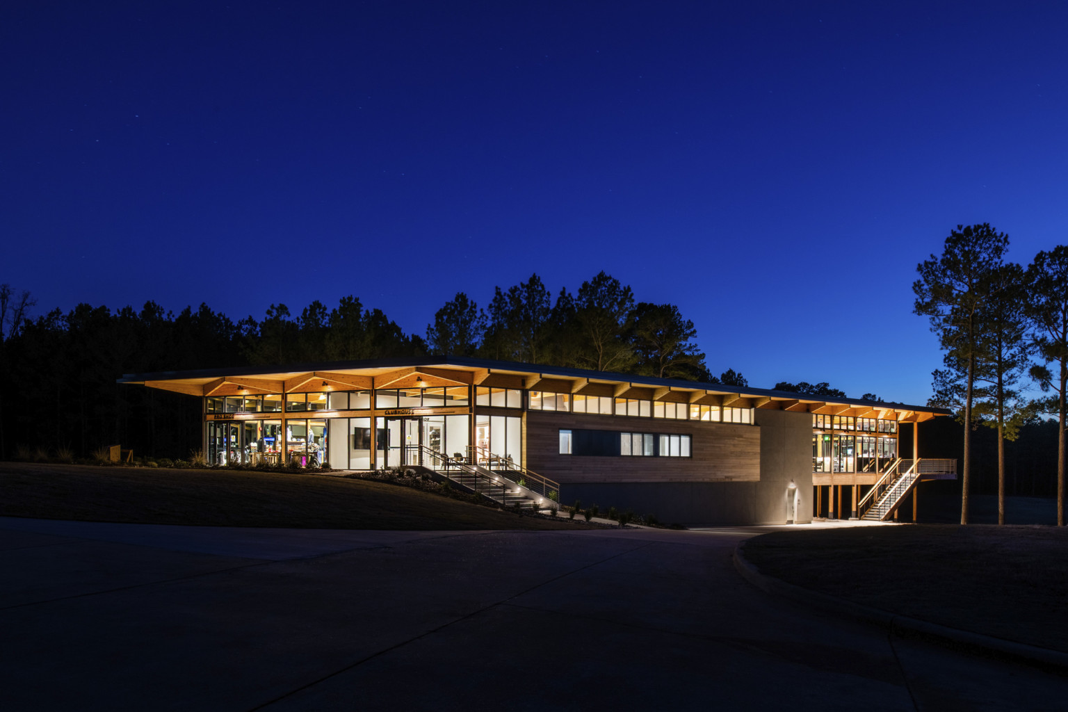 a two story exposed timber frame building with an all glass front set into a hillside along a treeline at night