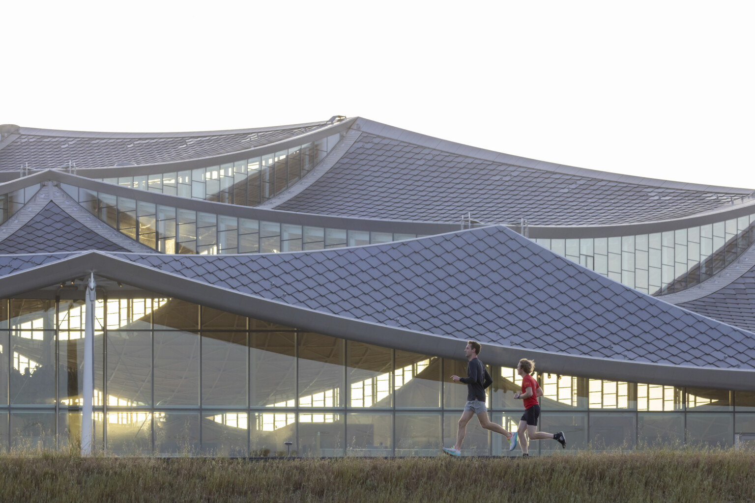 Two people running in front of a building with an all glass facade and rectangular glazing units and a tiled sloping roof; google bay view