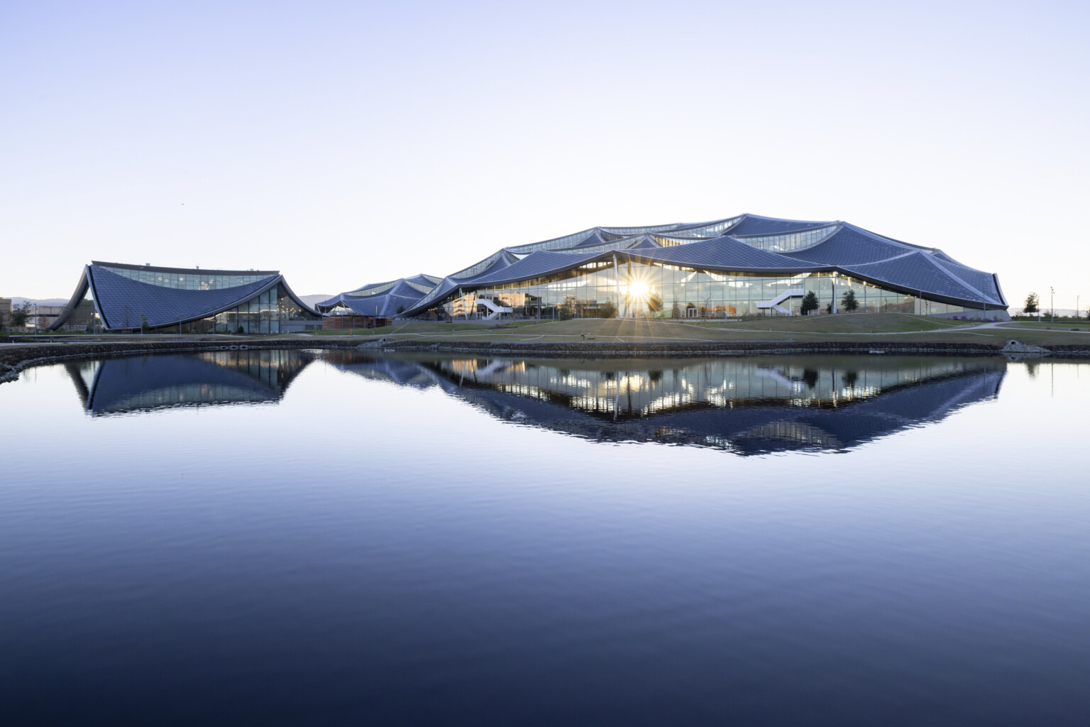 Three round buildings with rounded angular sloping roofs in a flat valley buildings reflected in a small body of water; google bay view
