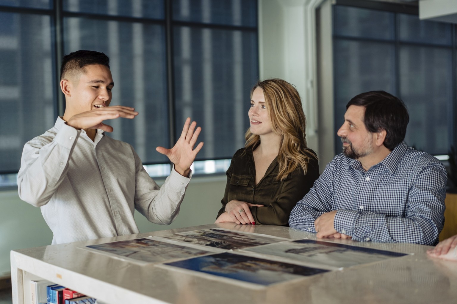 three designers standing around a table, teamwork, drawings on a table, sketches, windows to downtown