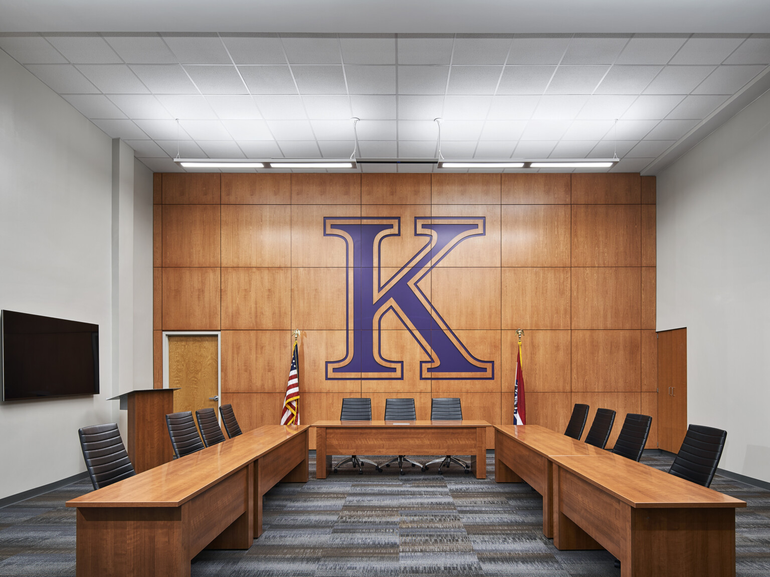 Boardroom with wood wall panels and embossed large purple K overlooking long tables with black office chairs facing center