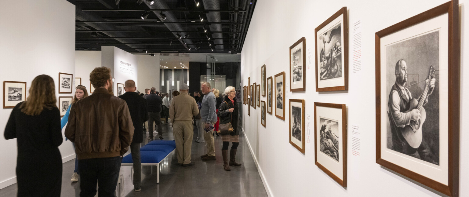People observing art in an art gallery with white walls and black ceiling, walls are filled with photographs People observing art in an art gallery with white walls and black ceiling, walls are filled with photographs