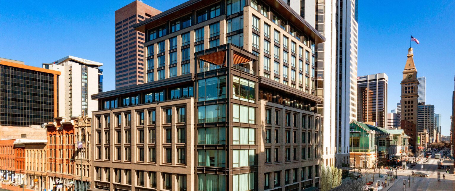 The Thompson Hotel Denver seen from corner with glass tower and stone facade on each side The Thompson Hotel Denver seen from corner with glass tower and stone facade on each side