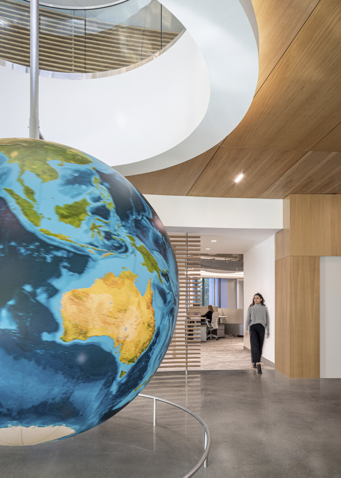 Curved hallway with floor to ceiling windows and wood panel ceiling. Round white recessed ceiling detail with hanging globe