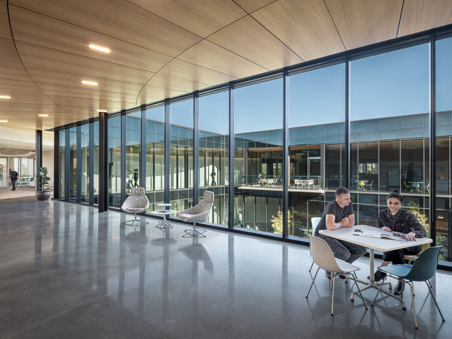 Floor to ceiling windows in squared U shape building. Mixed seating in office common space, room for collaboration, views to nature