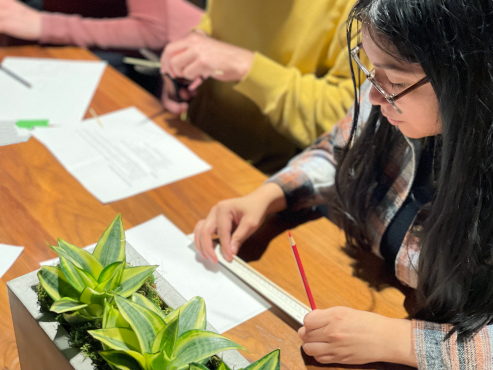 Female student sketching a diagram at a wooden table, mentorship program to introduce students to AEC industry