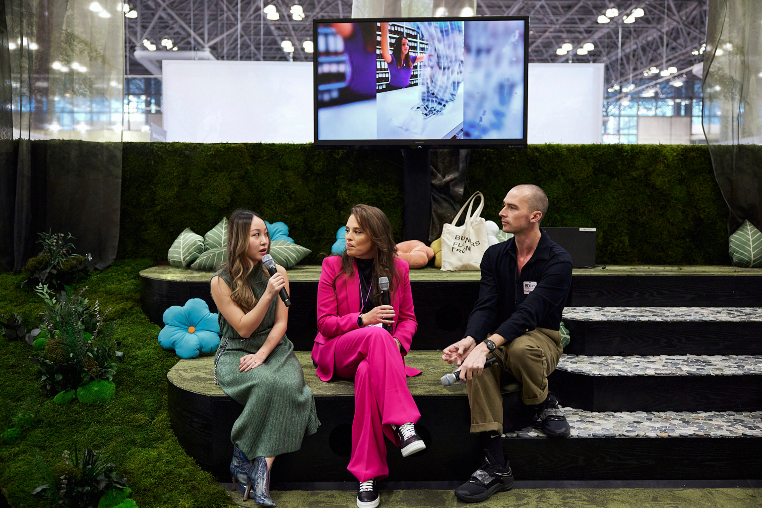 Two women and one man sitting in a custom booth delivering a presentation, booth designed with moss and flowers