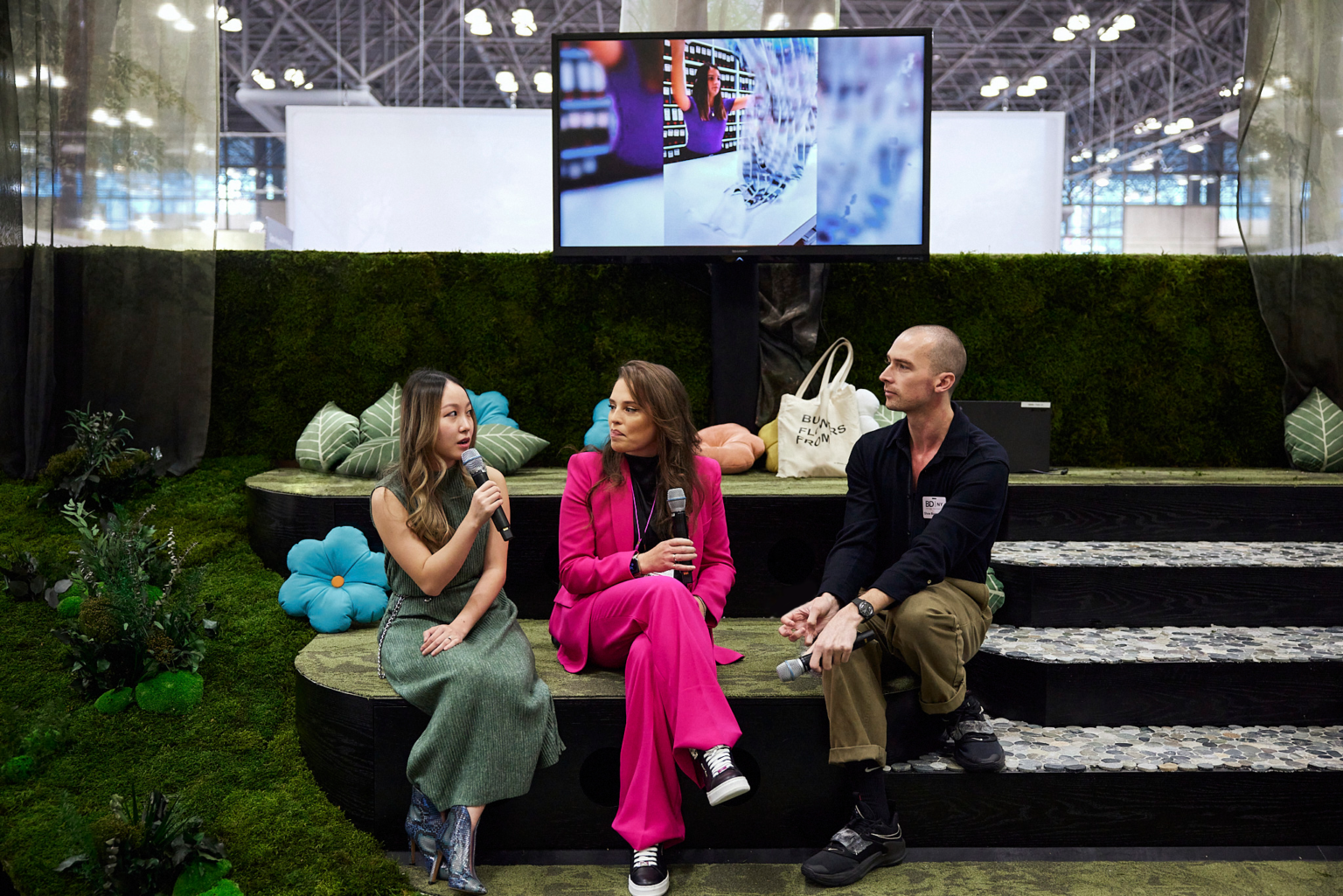 Two women and one man sitting in a custom booth delivering a presentation, booth designed with moss and flowers Two women and one man sitting in a custom booth delivering a presentation, booth designed with moss and flowers