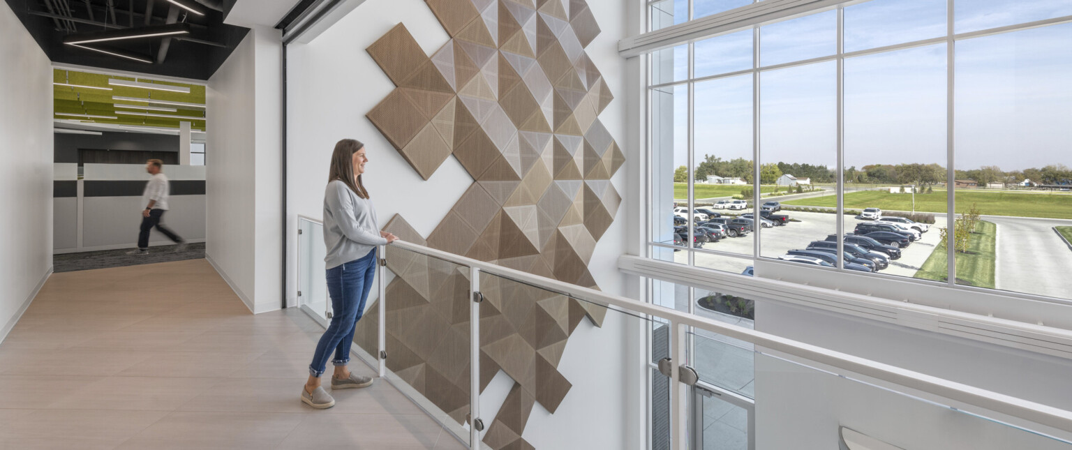 Second-floor view towards the three-story glass facade lobby. Accent wall with geometric wood panels in a random pattern.