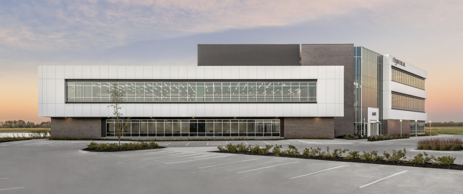 Rectangular pop out detail of the building façade with large windows. Parking lot in front