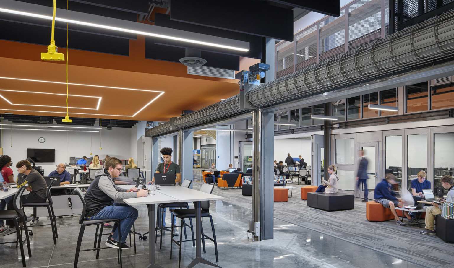 Large commons space with seating under a black ceiling and a geometric orange drop ceiling detail with recessed lights