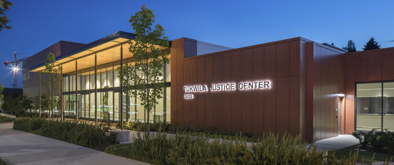 City of Tukwila Justice Center in the evening, with landscaping in the foreground. Single story double height glass facade building