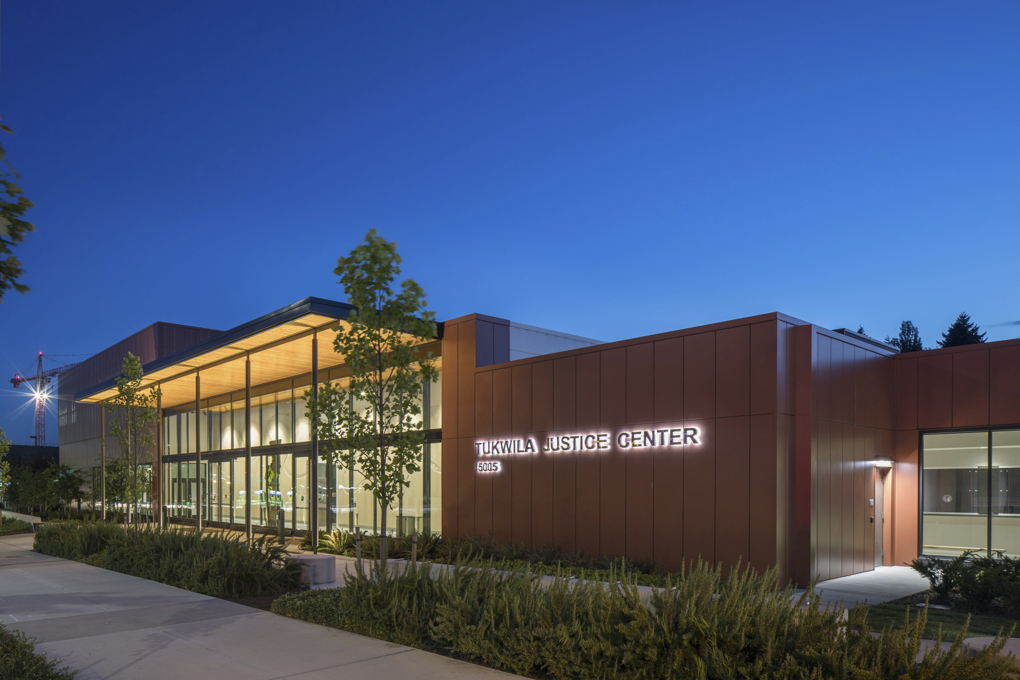 City of Tukwila Justice Center in the evening, with landscaping in the foreground. Single story double height glass facade building