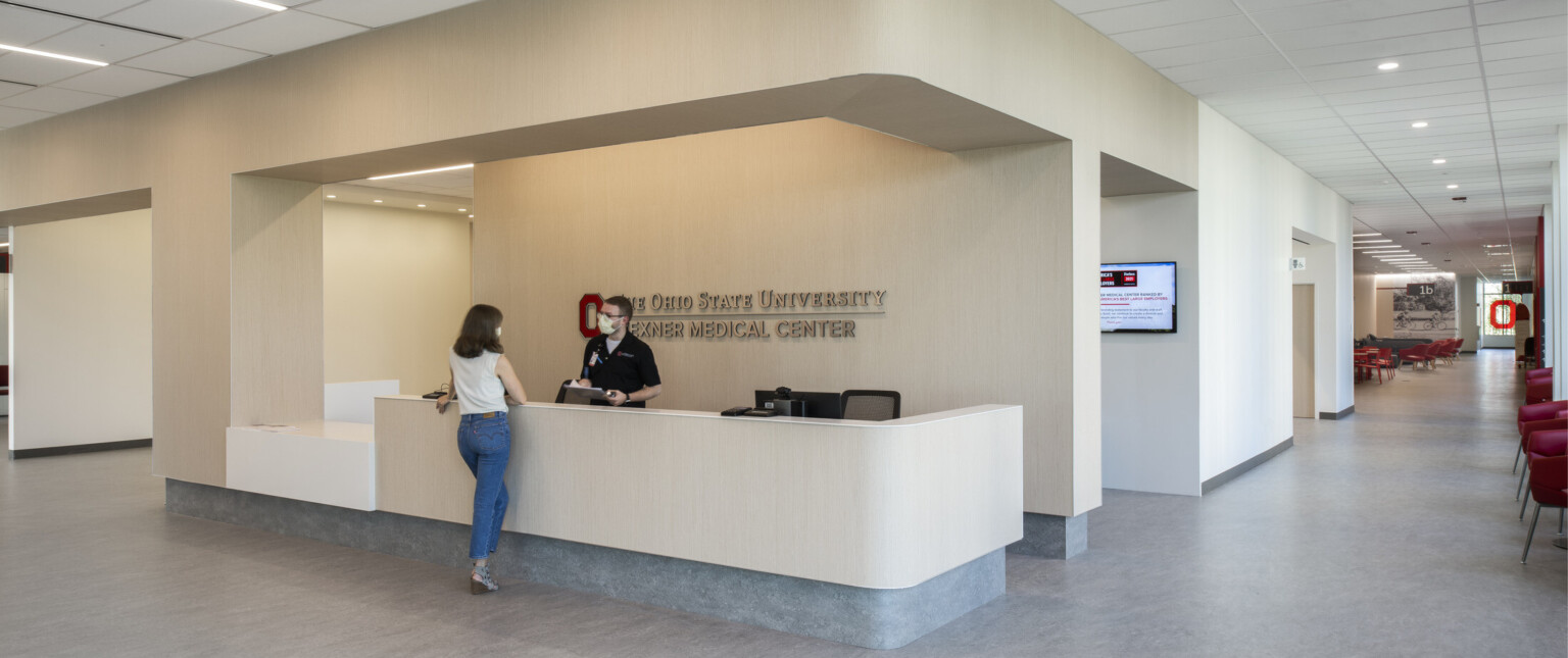 Entry reception desk in medical center. Beige desk matches wall colors, grey base matches floors. White panel ceiling