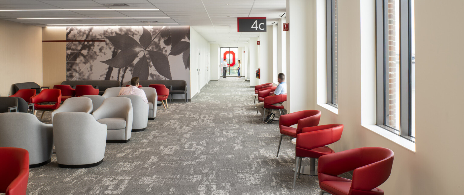 Waiting room area with textural grey carpe, black and white leaf photo mural, red and grey padded seating, large windows