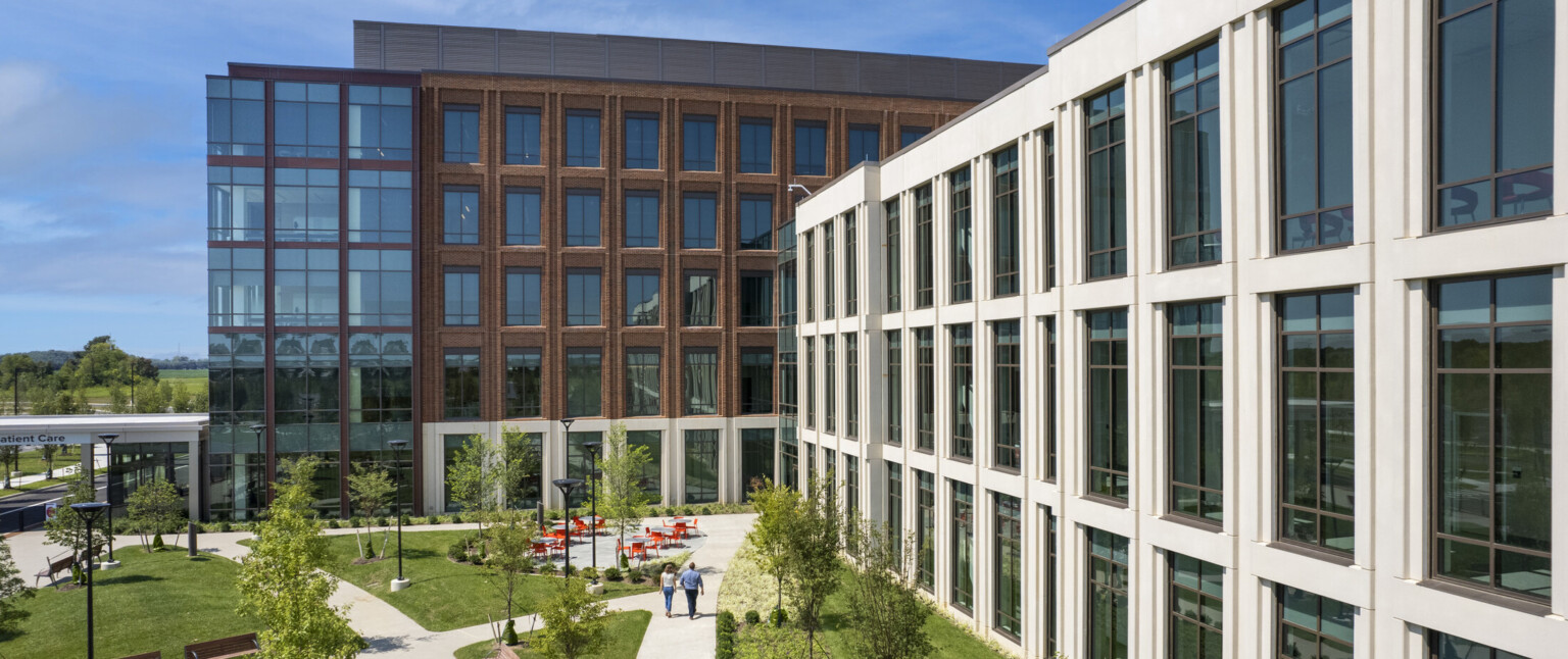 Courtyard with forking path in front of white building connecting to brick building with glass front entry facade to left