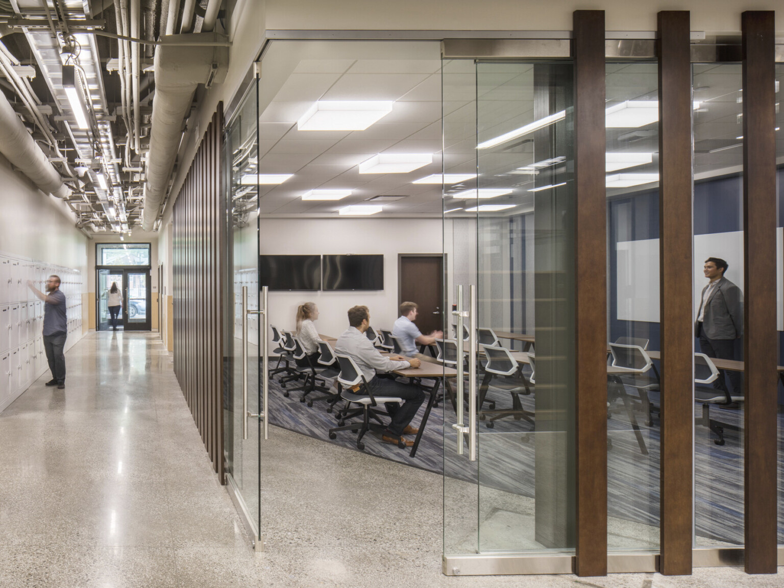 Glass walled classroom conference room with screens and white boards on wall with rows of flexible tables and office chairs