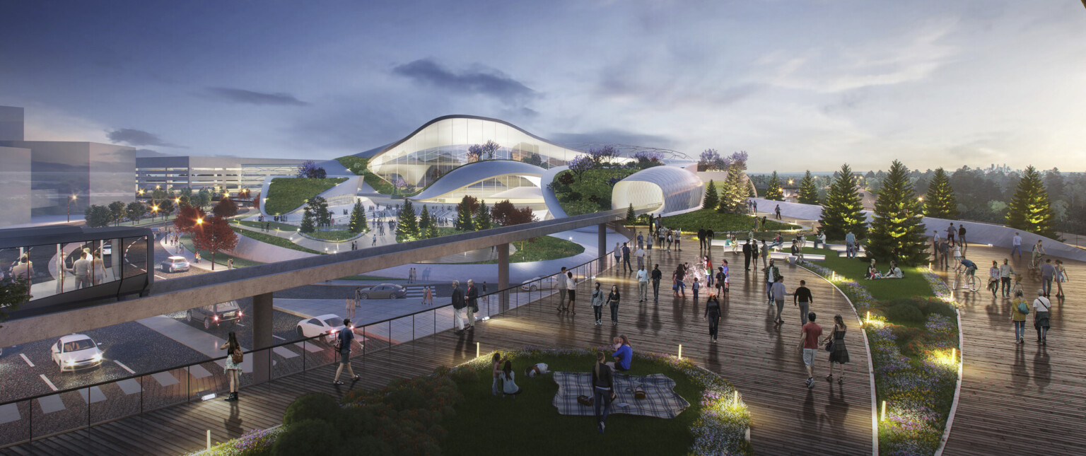 White building with rounded flowing walls and multiple stories in green space with lots of trees and Expo 2027 sign