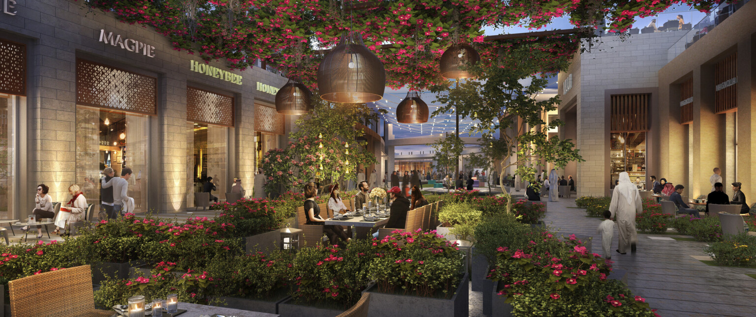 Partially covered outdoor shopping center, planters and tables at center. Pendant lights with brown shades hang from trellises