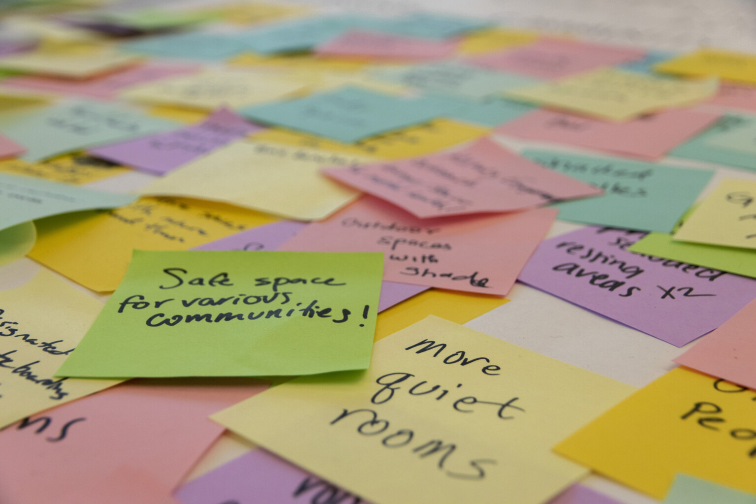 Large pile of overlapping multi-colored post-it notes with ideas written in black marker