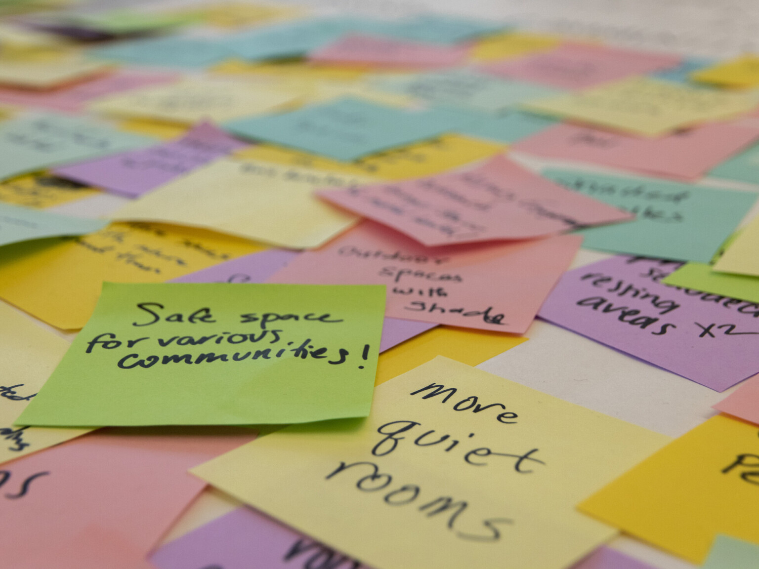 Large pile of overlapping multi-colored post-it notes with ideas written in black marker