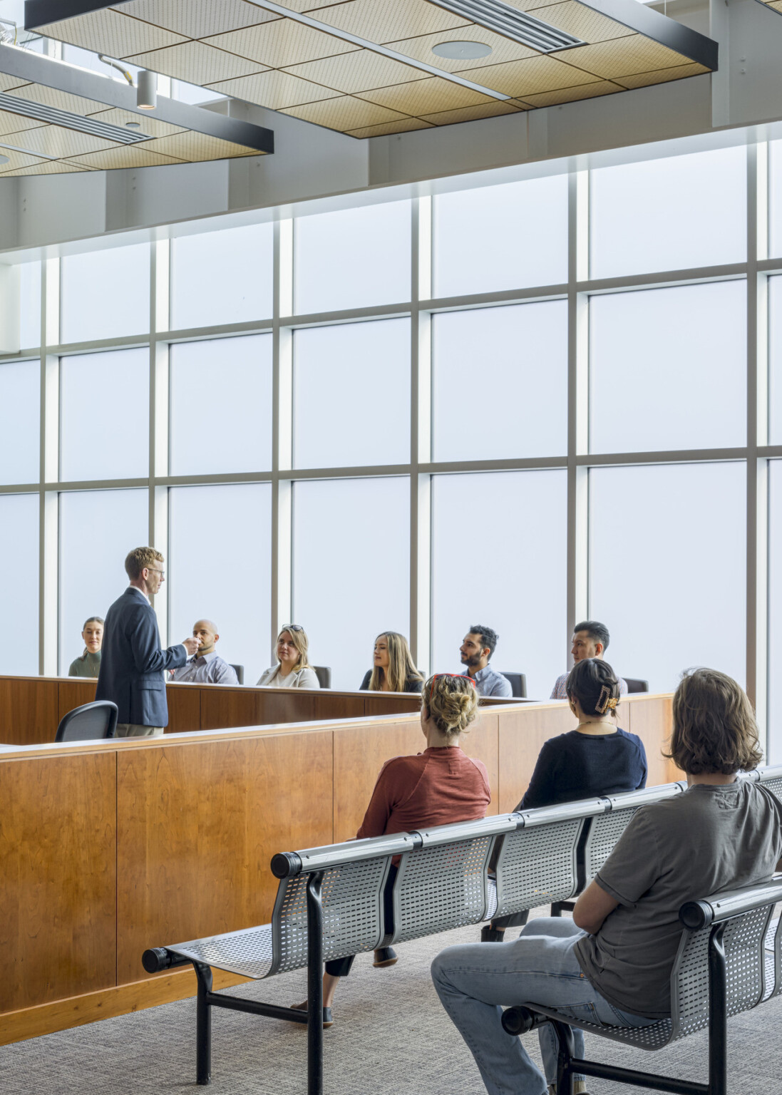 Warm wood tones and expansive windows welcome the public and convey transparency of government, comfortable seating in courtroom