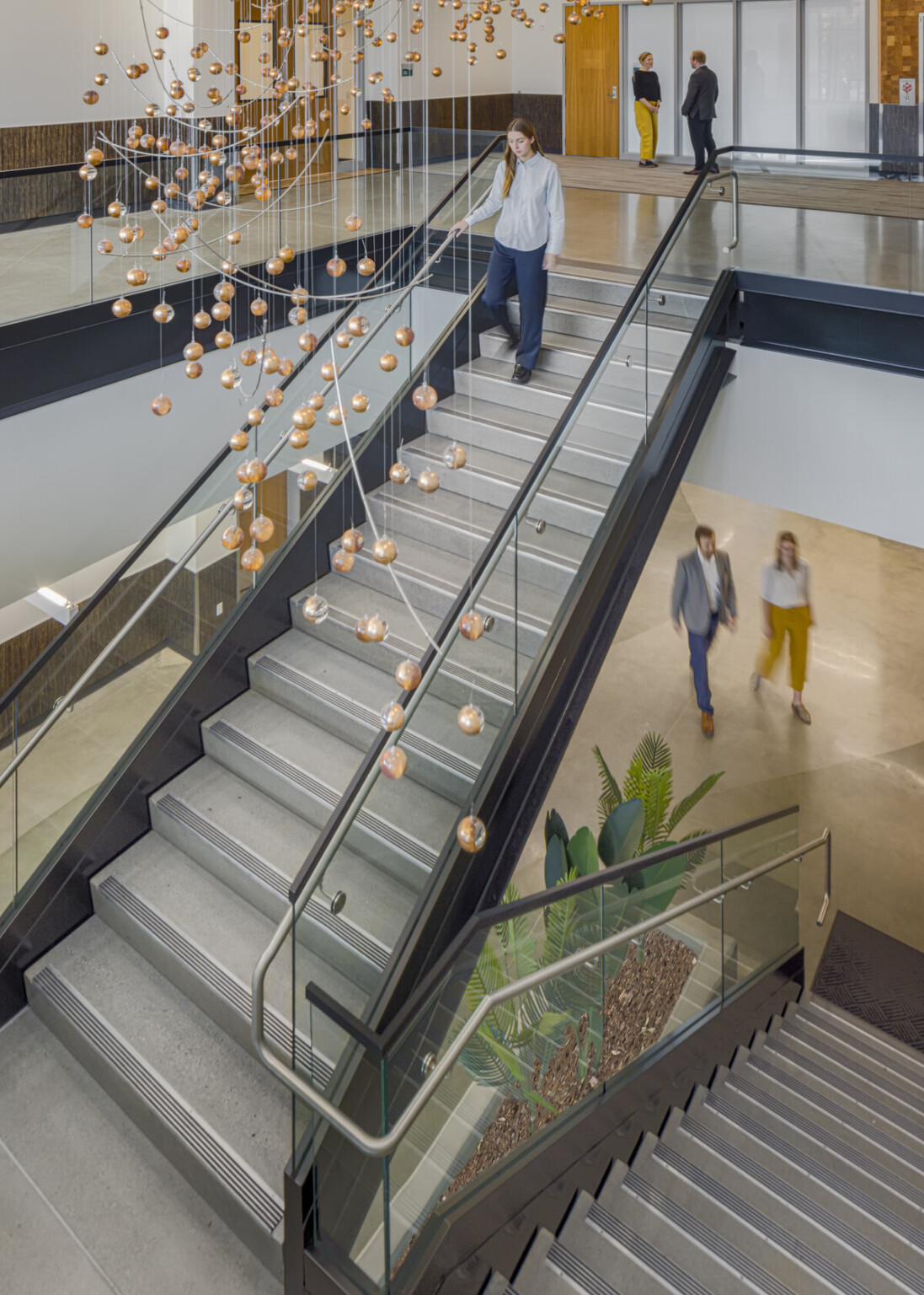 Aeriel view of the glass and metal stairway with black accents, modern art mobile sculpture with bronze spheres, plants