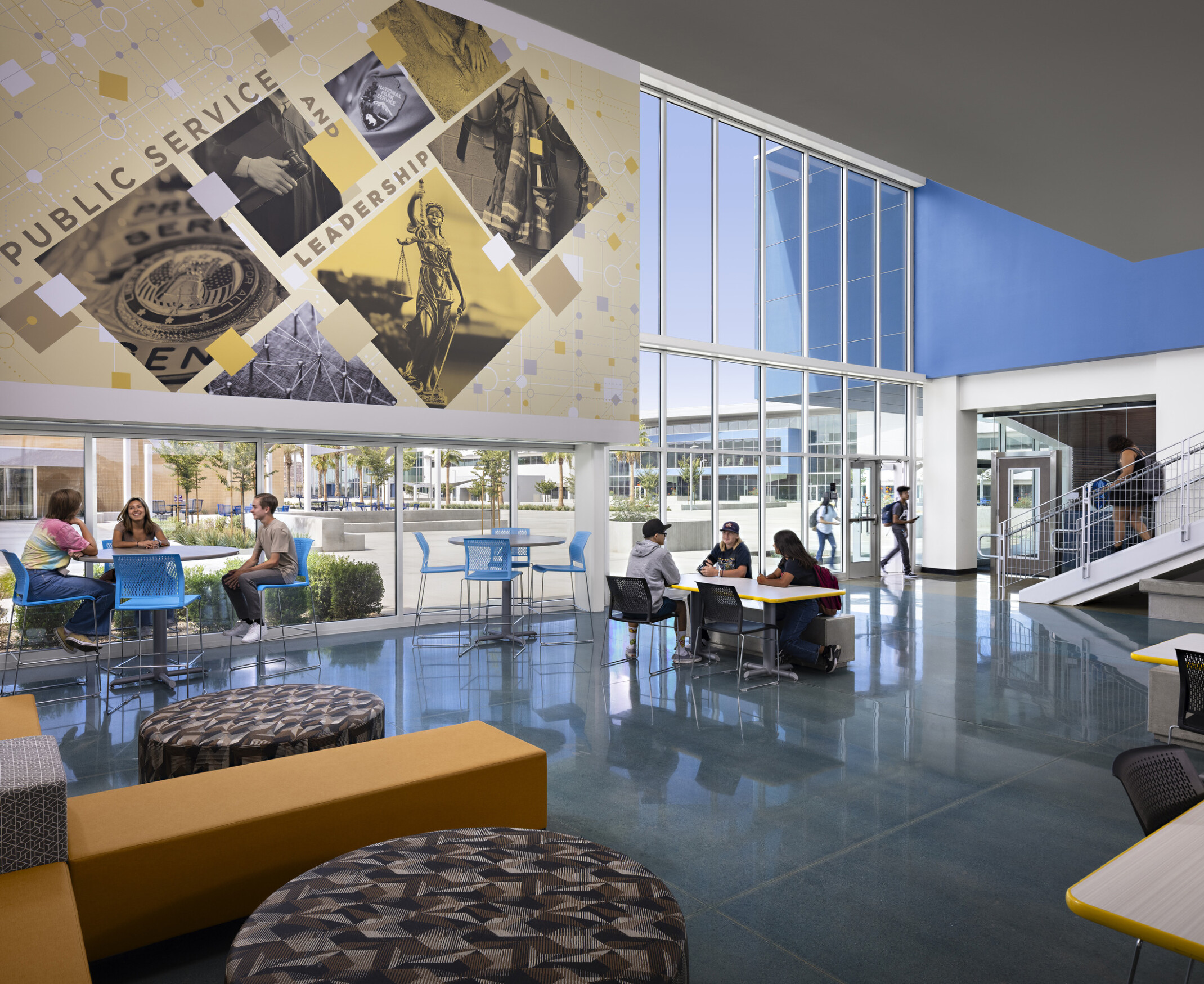 Interior double height 1st floor seating area of Liberty high school; view to courtyard; Colorful high school design; geometric yellow toned photo mural; blue accent wall