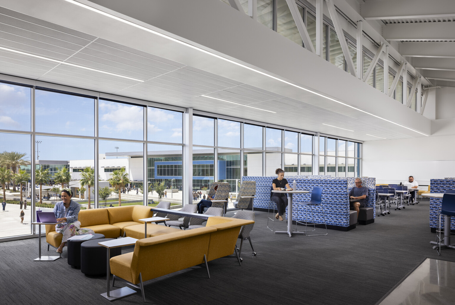 Upper level mixed seating area with orange couches and blue booths and stools in common space with tables to work on homework