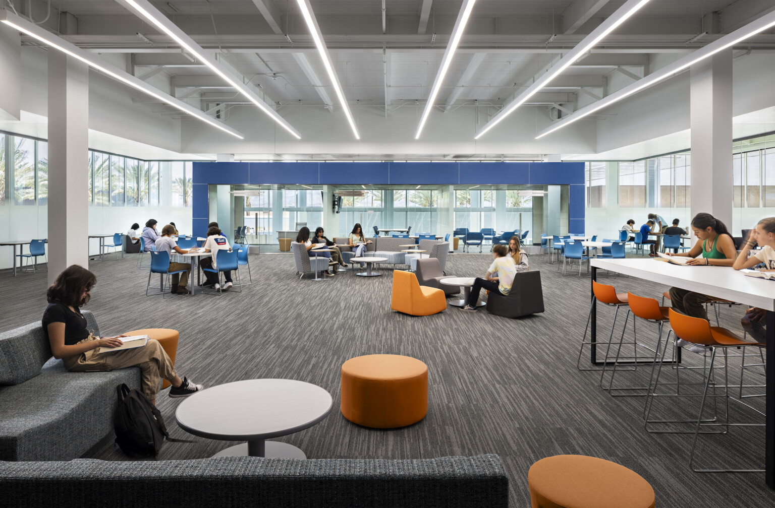 Mixed comfortable seating in common area with walls of windows surrounding room, white ceiling, blue and orange accents