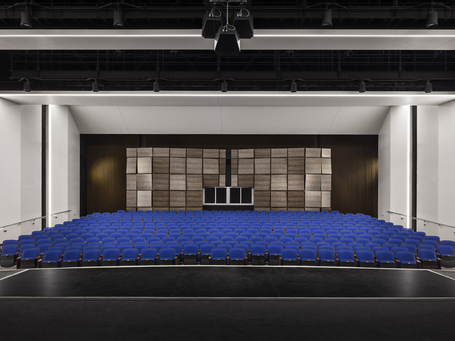 View from stage looking towards audience chamber with blue eats and white walls, textured acoustical panels on back wall