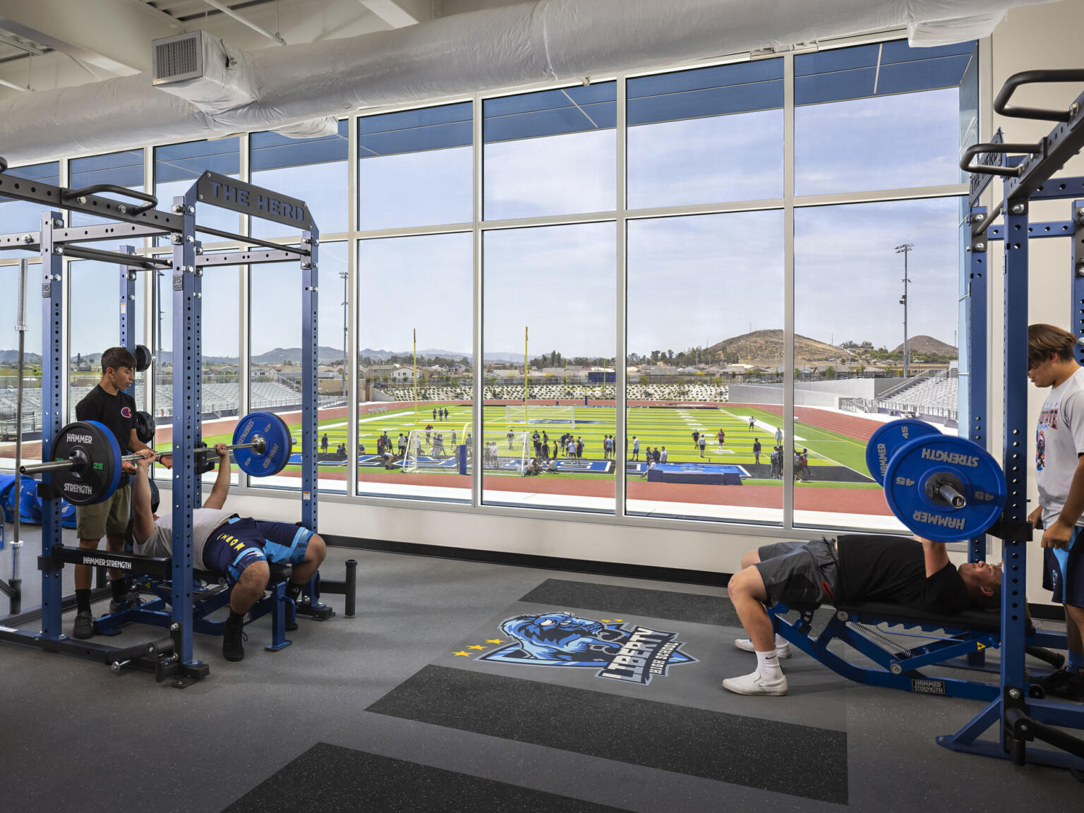 Exercise room with weight training equipment, floor to ceiling windows look out to football field and track