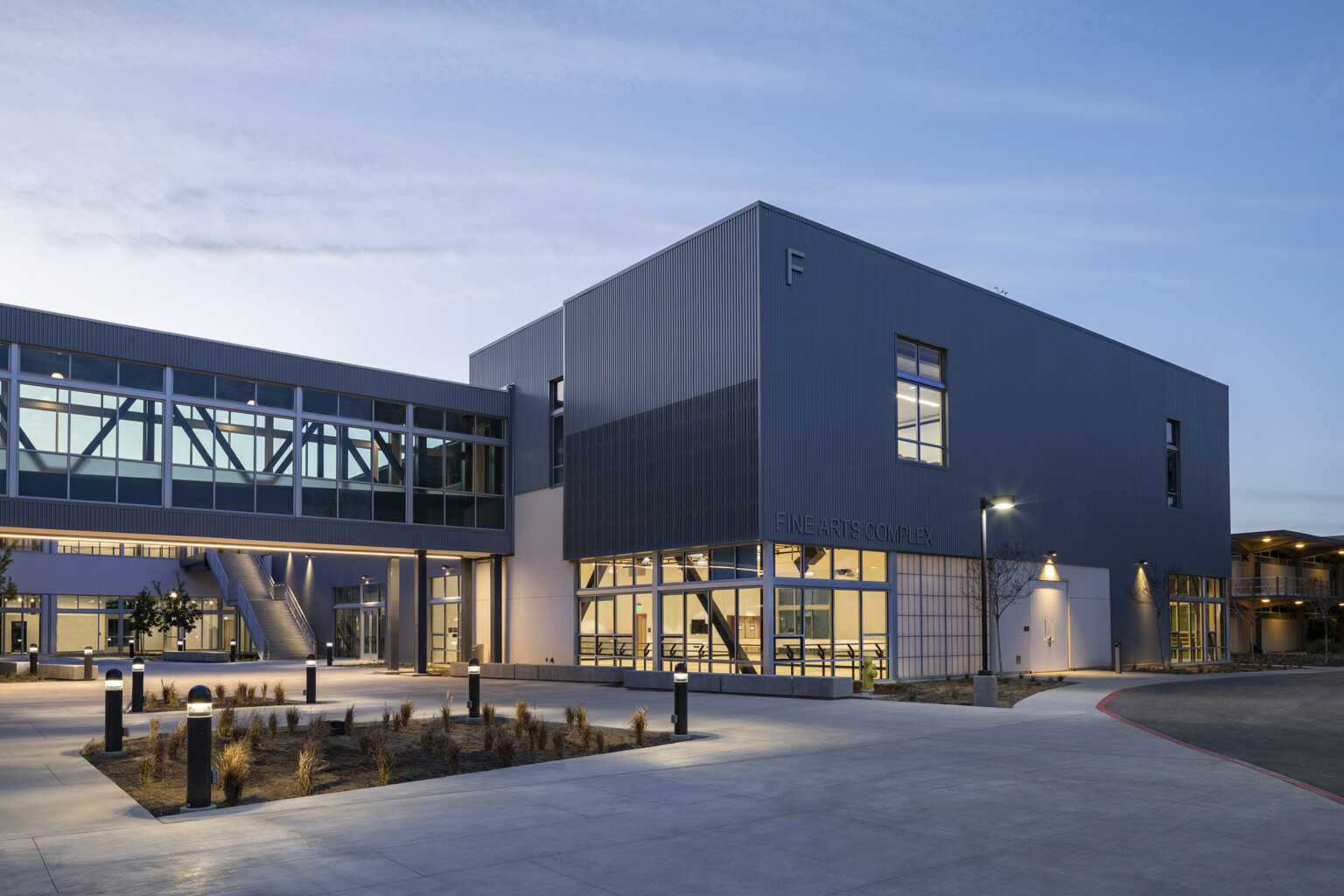 Modern metal construction, sky bridge connects other structures for collaboration, daylit, floor-to-ceiling windows on ground level at dusk