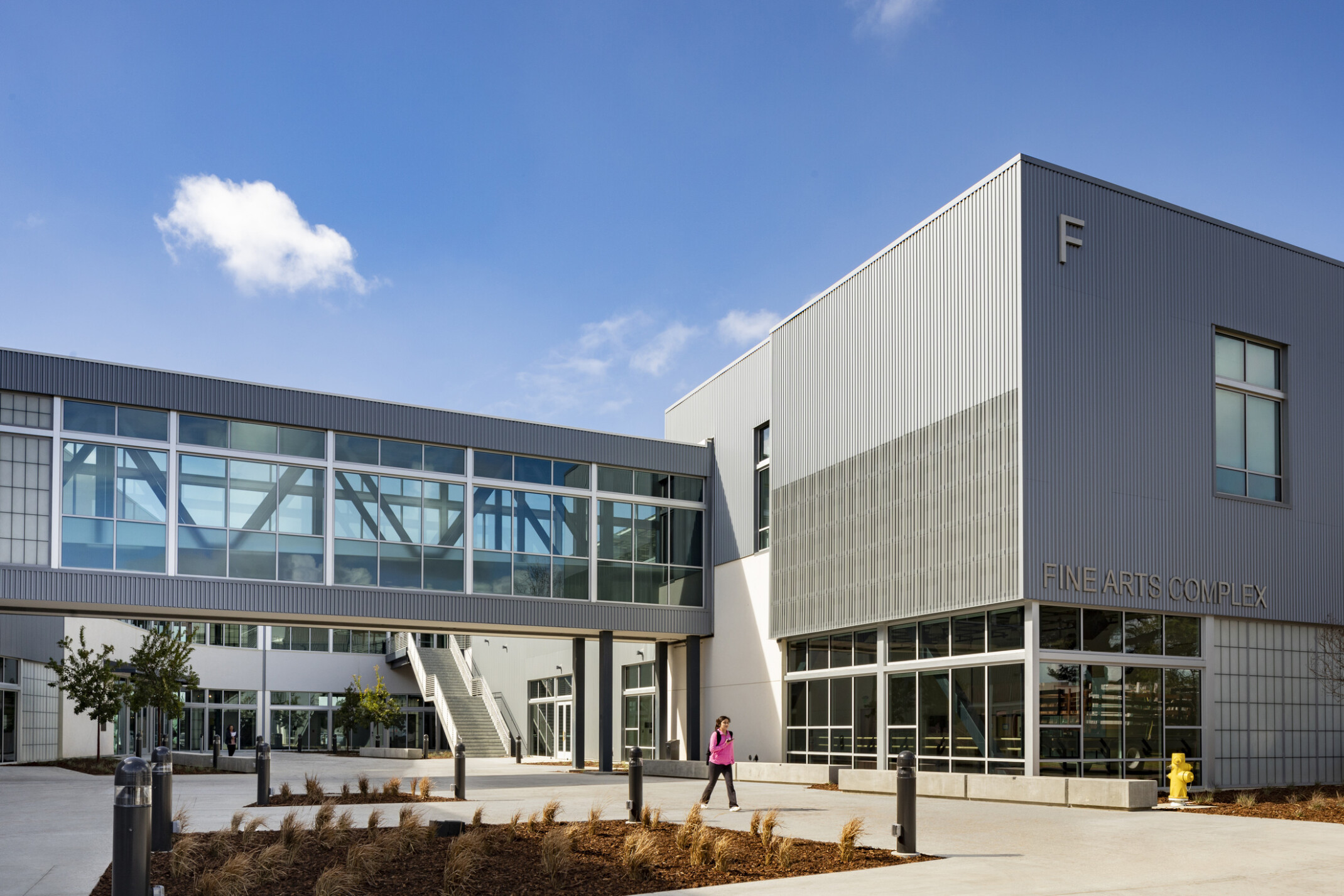 Modern metal construction, sky bridge connects other structures for collaboration, daylit, floor-to-ceiling windows on ground level, natural ventilation, and indoor/outdoor connections, the building maximizes sustainability and well-being for its users