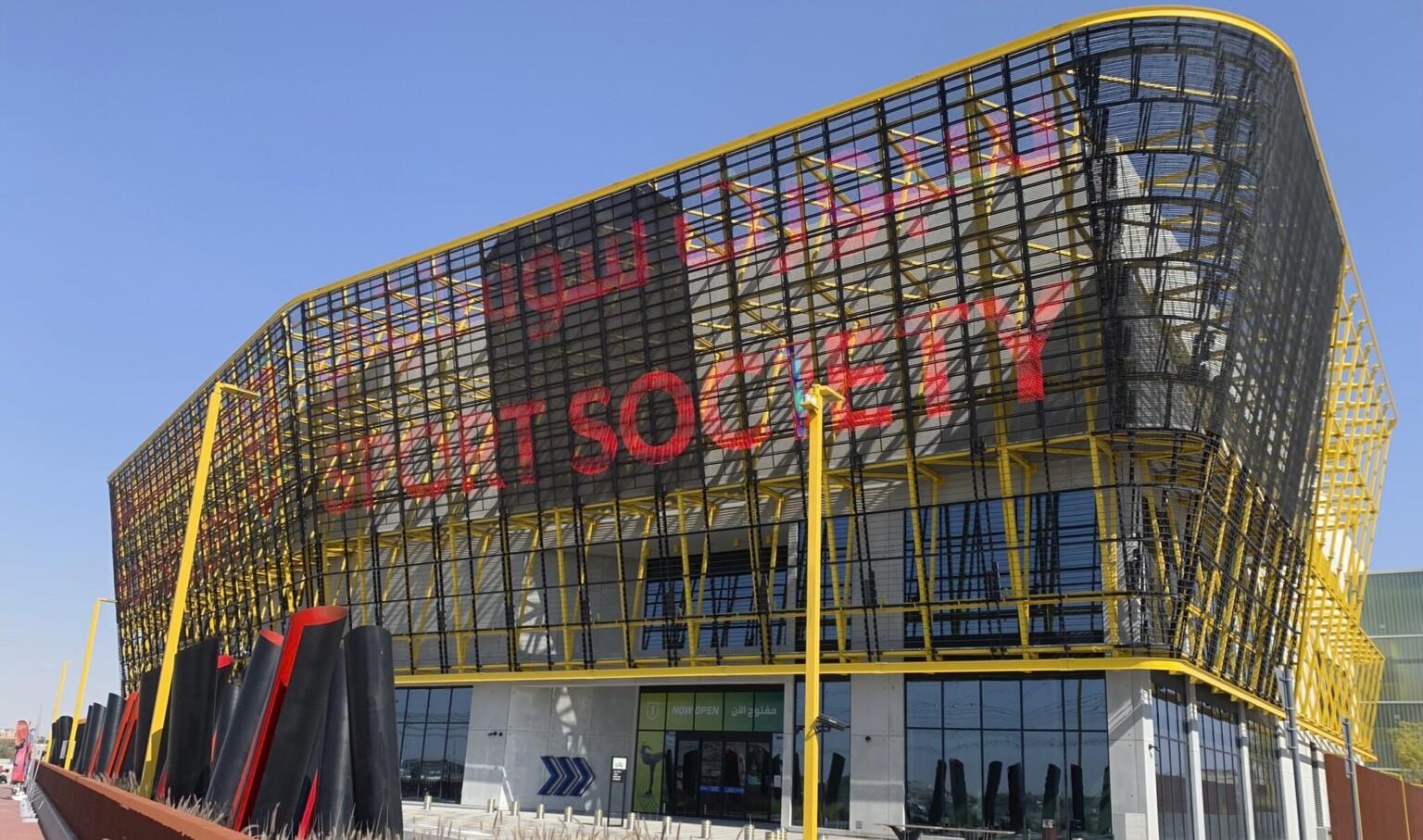 Entrance at Sport Society building with steel frame and red writing with yellow accents