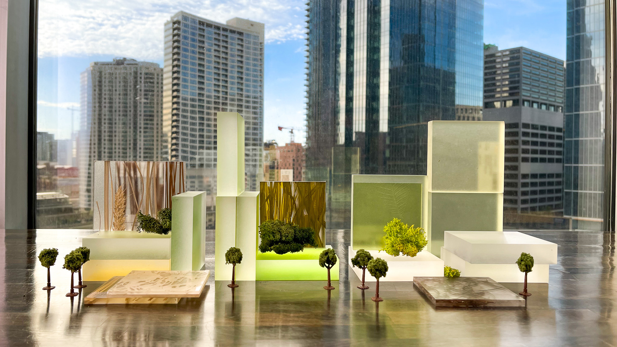 green toned abstract clear models of building with scale trees in front of window, view of high rises green toned abstract clear models of building with scale trees in front of window, view of high rises