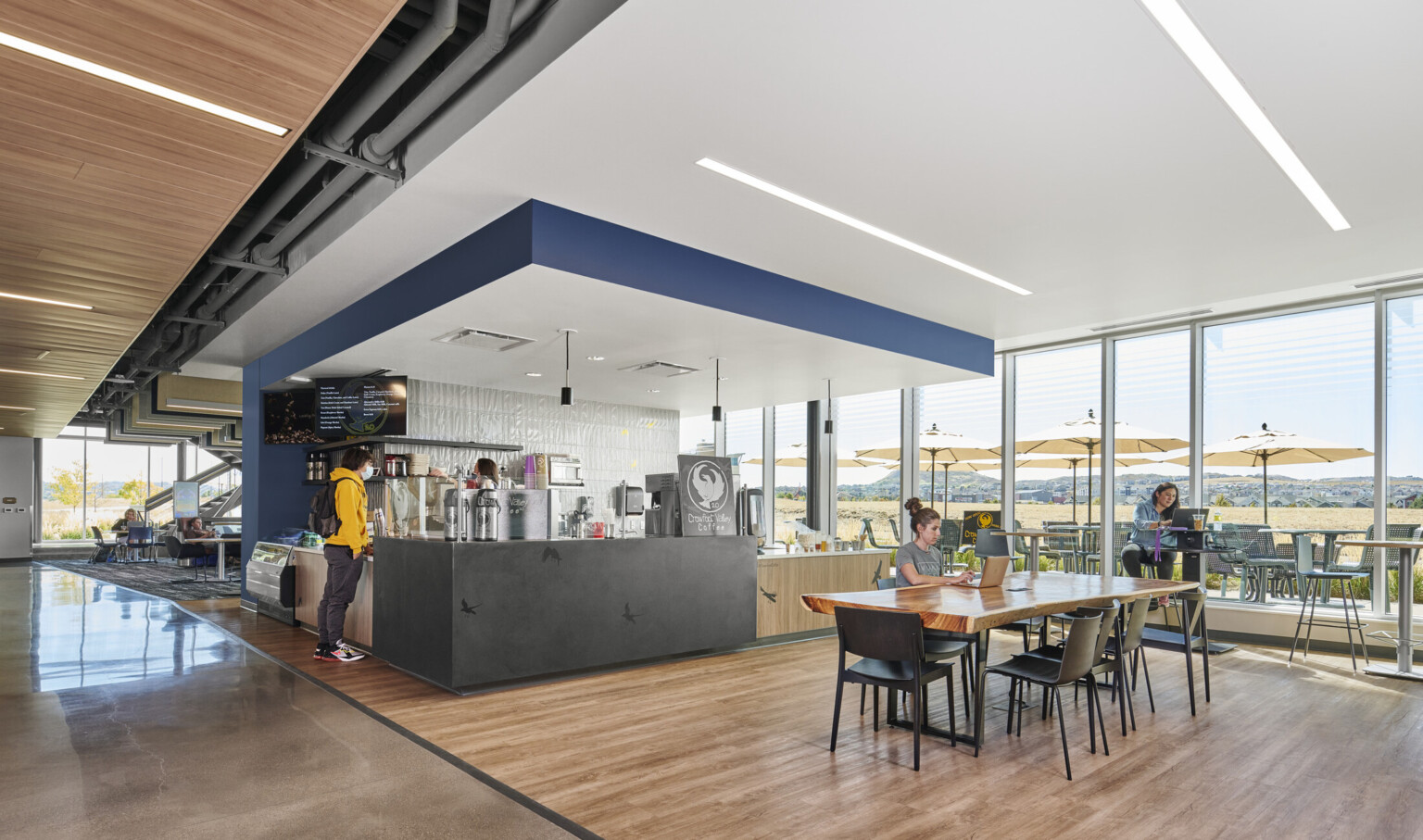 Floor to ceiling windows look out to Colorado landscape, patio seating, student café, study tables, wood, bright, open, airy, welcoming, inviting, sunny