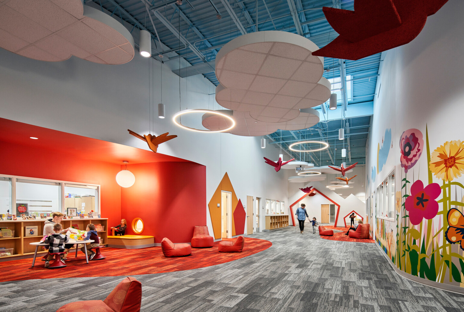 high blue ceilings and grey geometric print carpet with suspended cloud and orange bird elements, bright orange accent wall, mural with brightly colored flowers