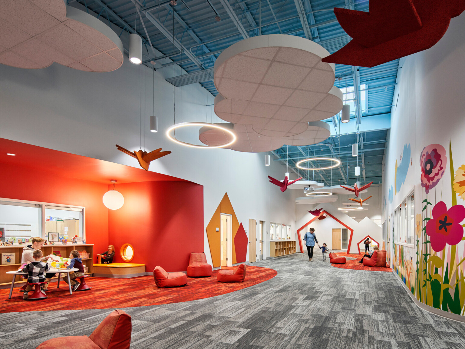 high blue ceilings and grey geometric print carpet with suspended cloud and orange bird elements, bright orange accent wall, mural with brightly colored flowers