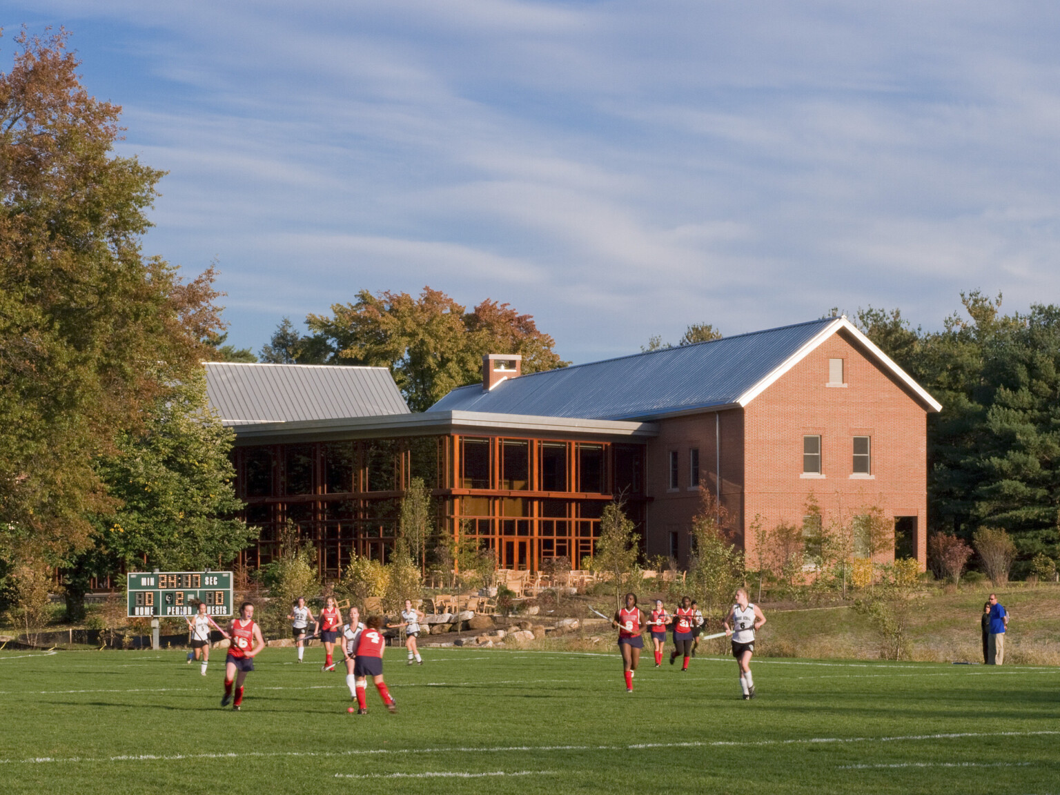 Exterior of library and learning commons double height glass facade viewed from across field as girls play field hockey