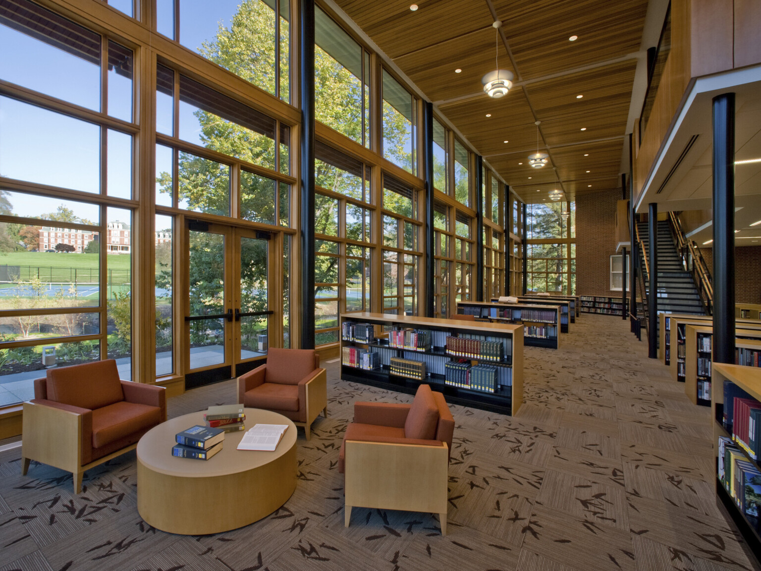 Double height library seating area with half height shelves and armchair seating, glass facade with wood accents