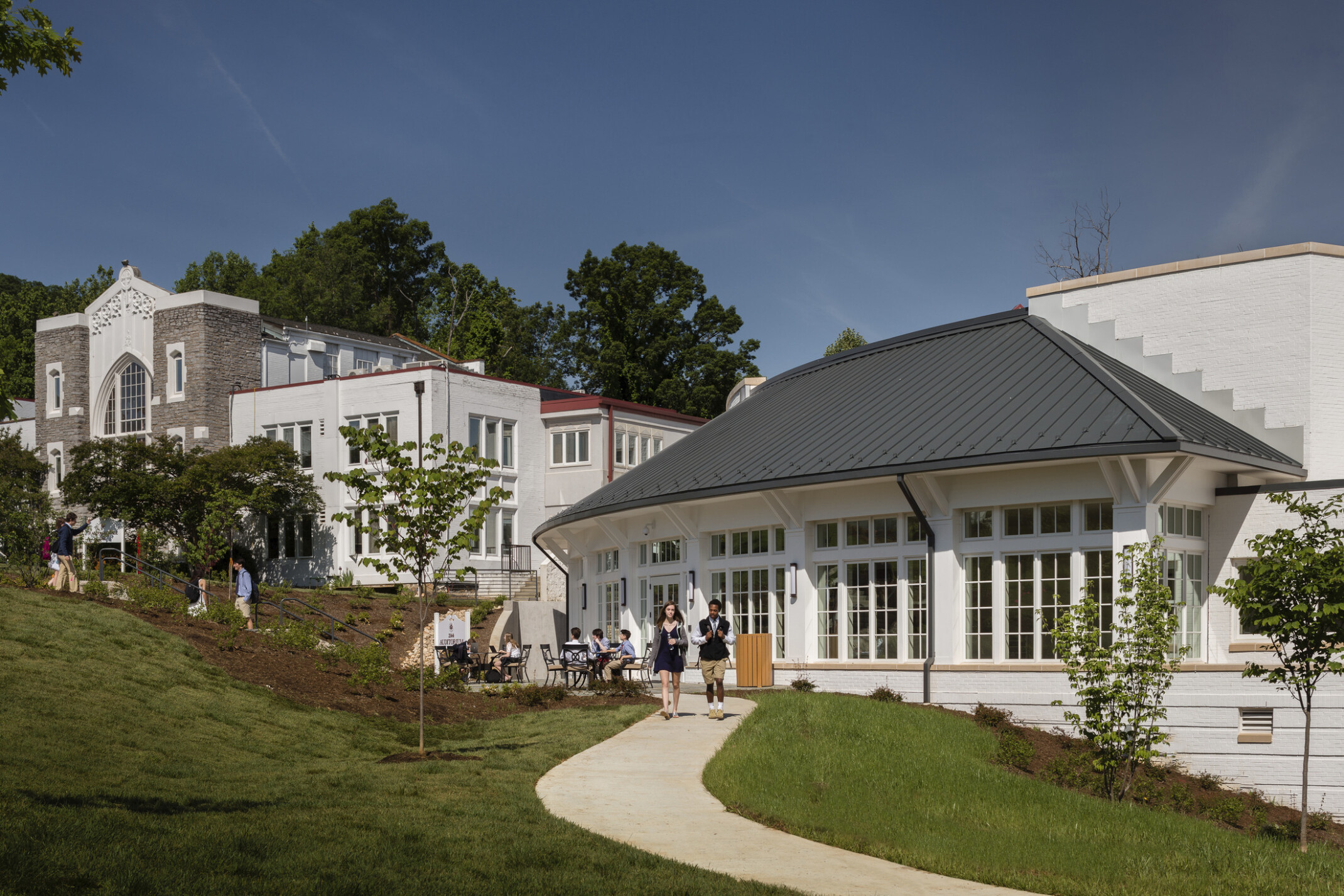 St. Anne’s-Belfield School's Grisham Hall Auditorium exterior, white 1 story building with windows on rounded canopied entry wall