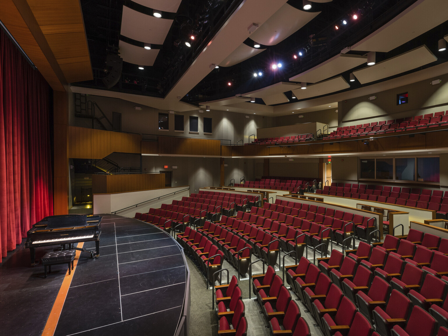 Double height auditorium theater looking across stage and audience chamber, right, brown acoustic panels above, lighting equipment