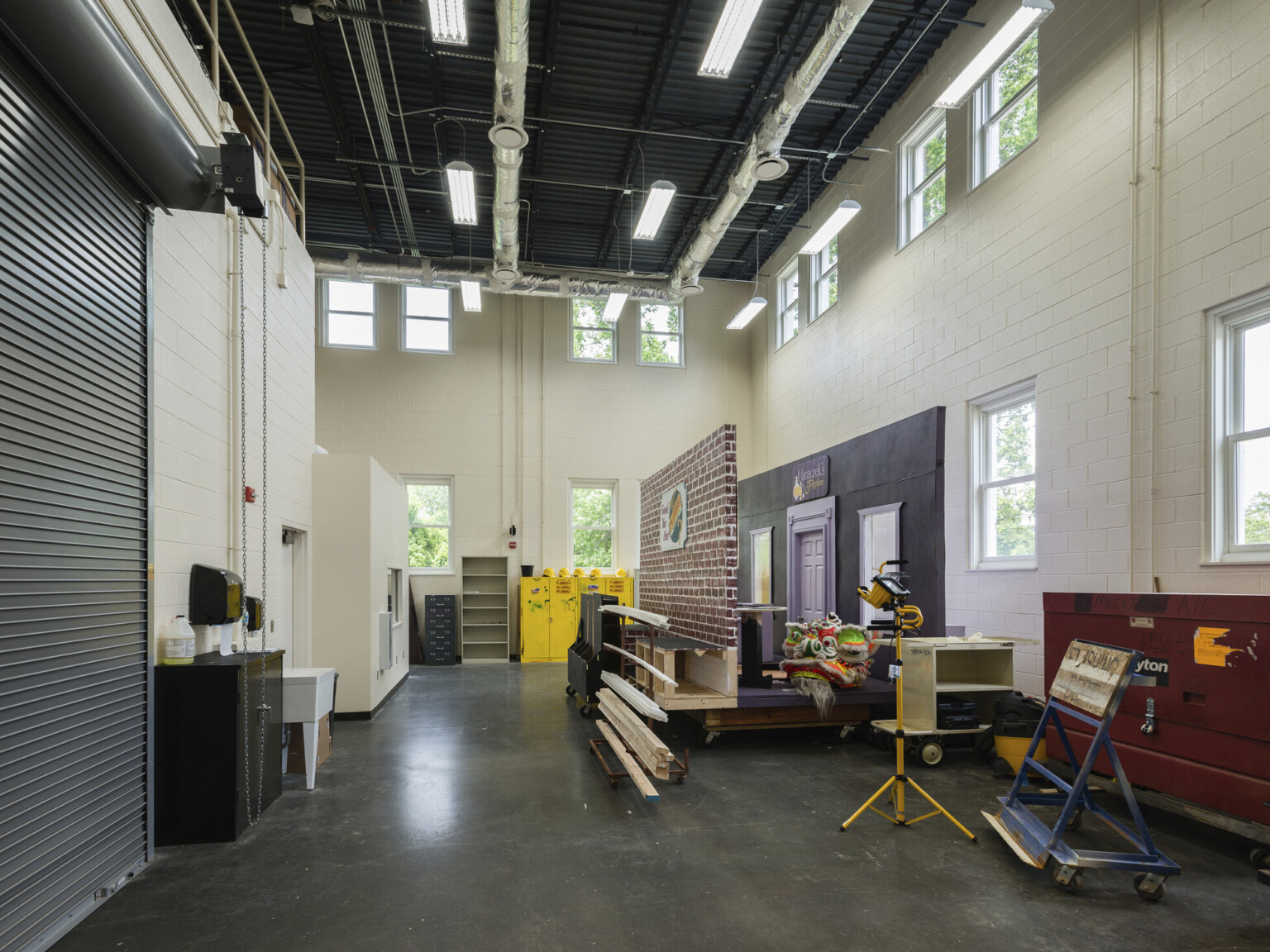 Double height back storage room with workspace, tall garage door, windows bringing in natural light, lockers and scenery