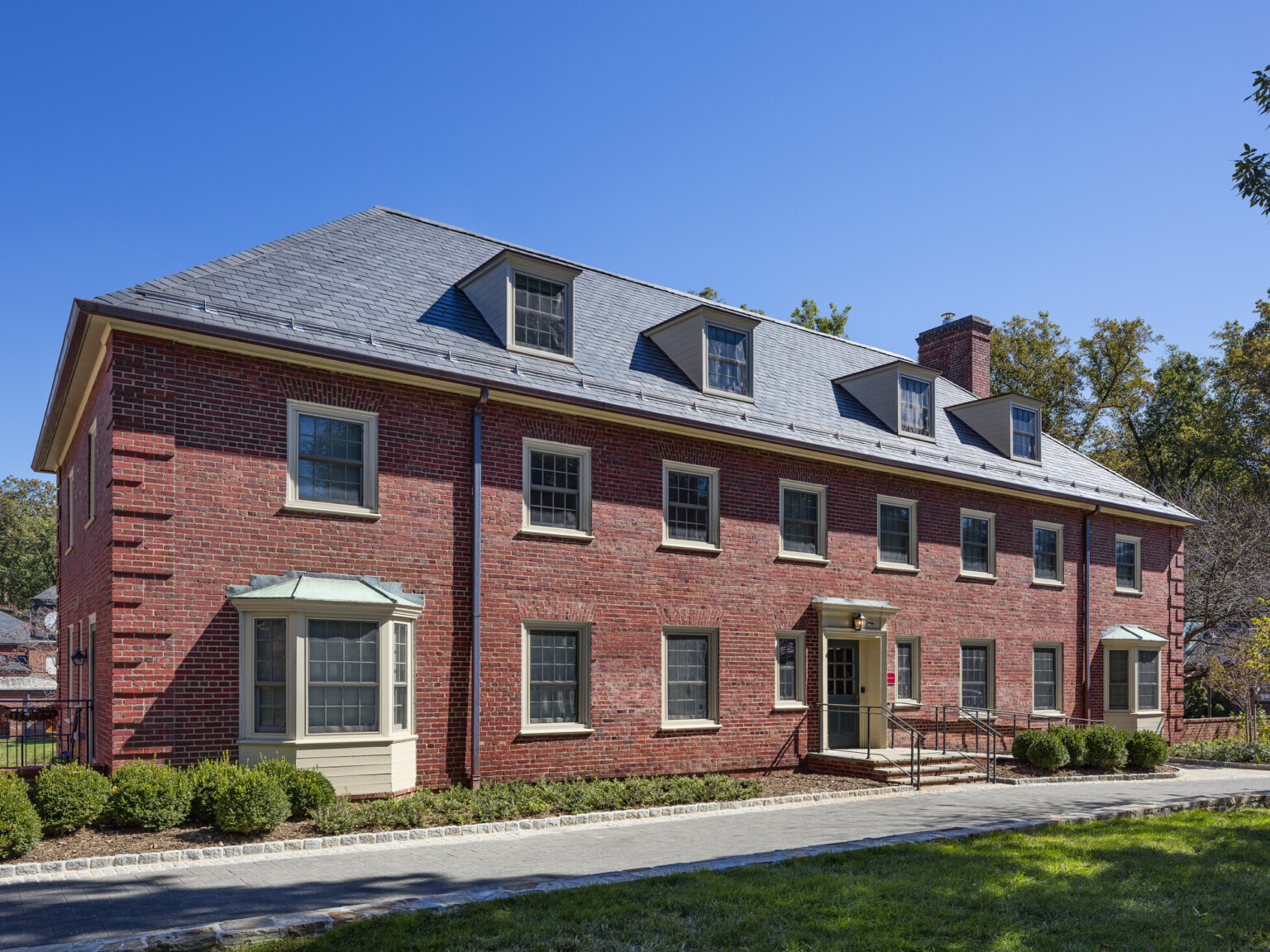 exterior view of three-story Georgian inspired brick dormitory building, blue skies, landscaping, tall trees and grassy knoll