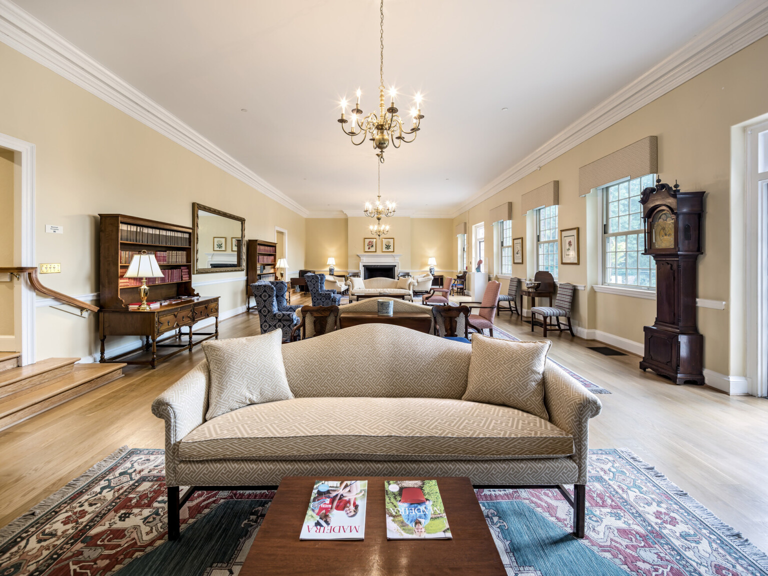 ground level visitor room with multiple seating areas, wing-back chairs, settees, coffee tables, grandfather clock, chandelier