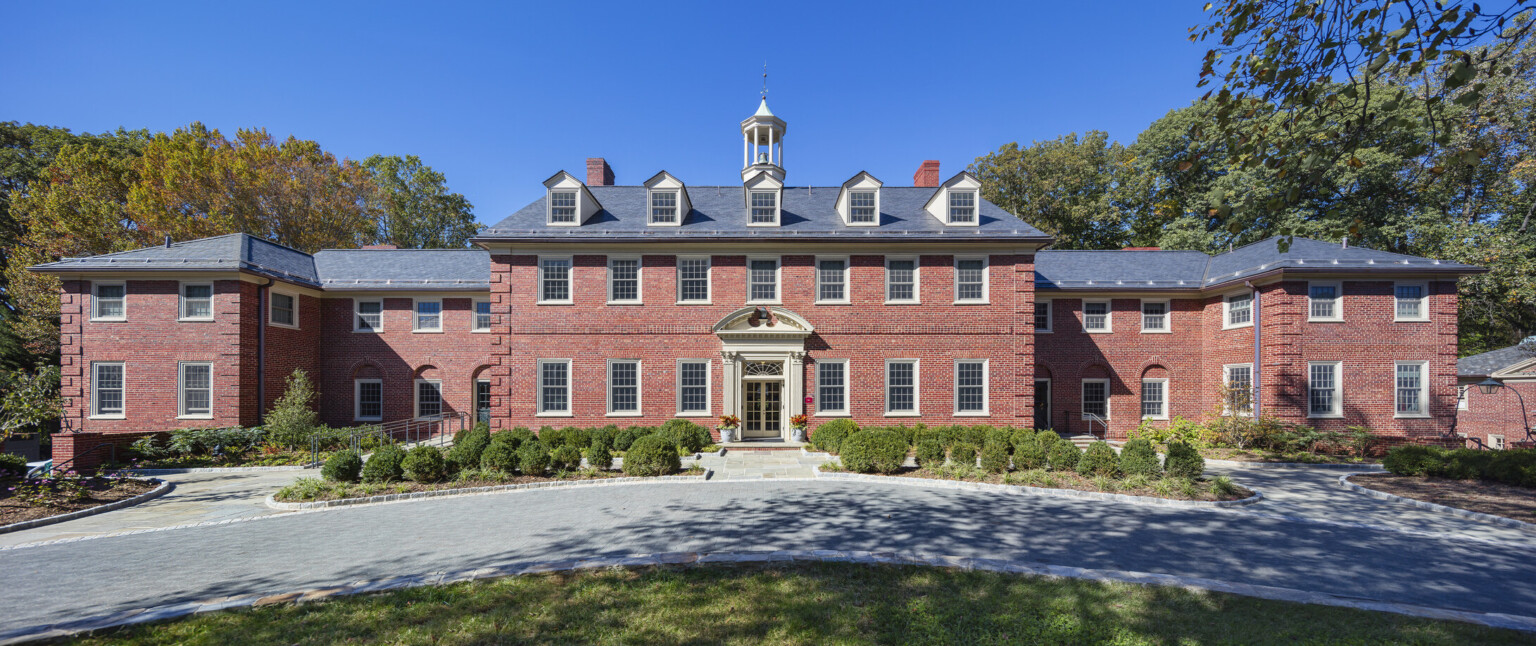 exterior view of three Georgian inspired brick dormitory buildings, parking lot, entrance, blue skies, landscaping, tall trees and grassy knoll