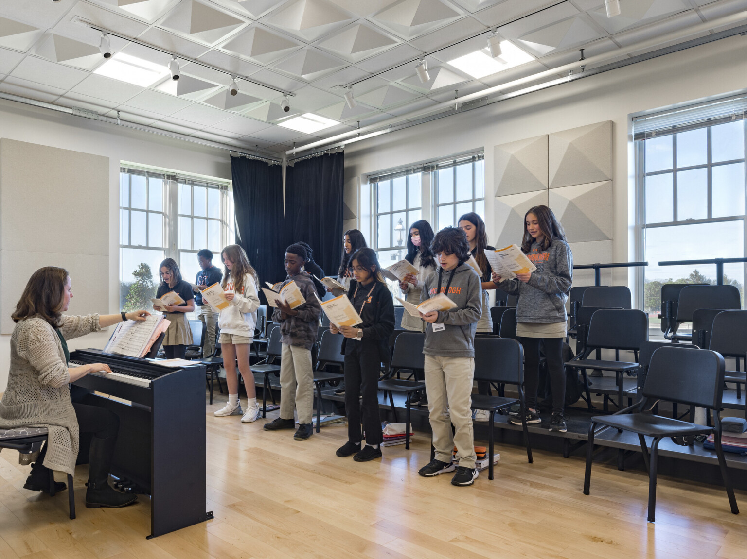 Students and instructor in classroom with chairs on risers and black curtains hanging along walls, geometric acoustic panels on ceiling